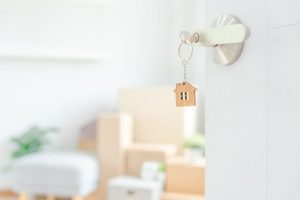 Keys in the lock of an open door in the foreground and cardboard moving boxes in the background.